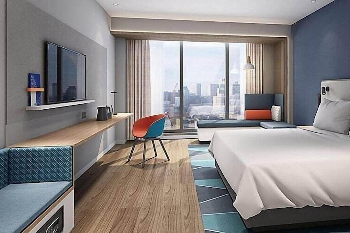 Habitación de hotel moderna con una cama grande, zona de estar, televisor y vista a la ciudad.