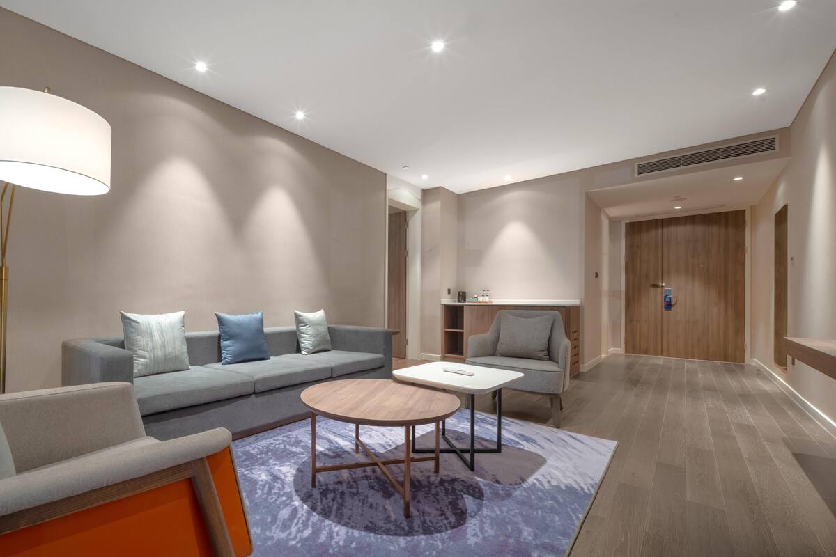 Una habitación de hotel moderna con sofá, sillón, mesa de centro redonda y una lámpara.