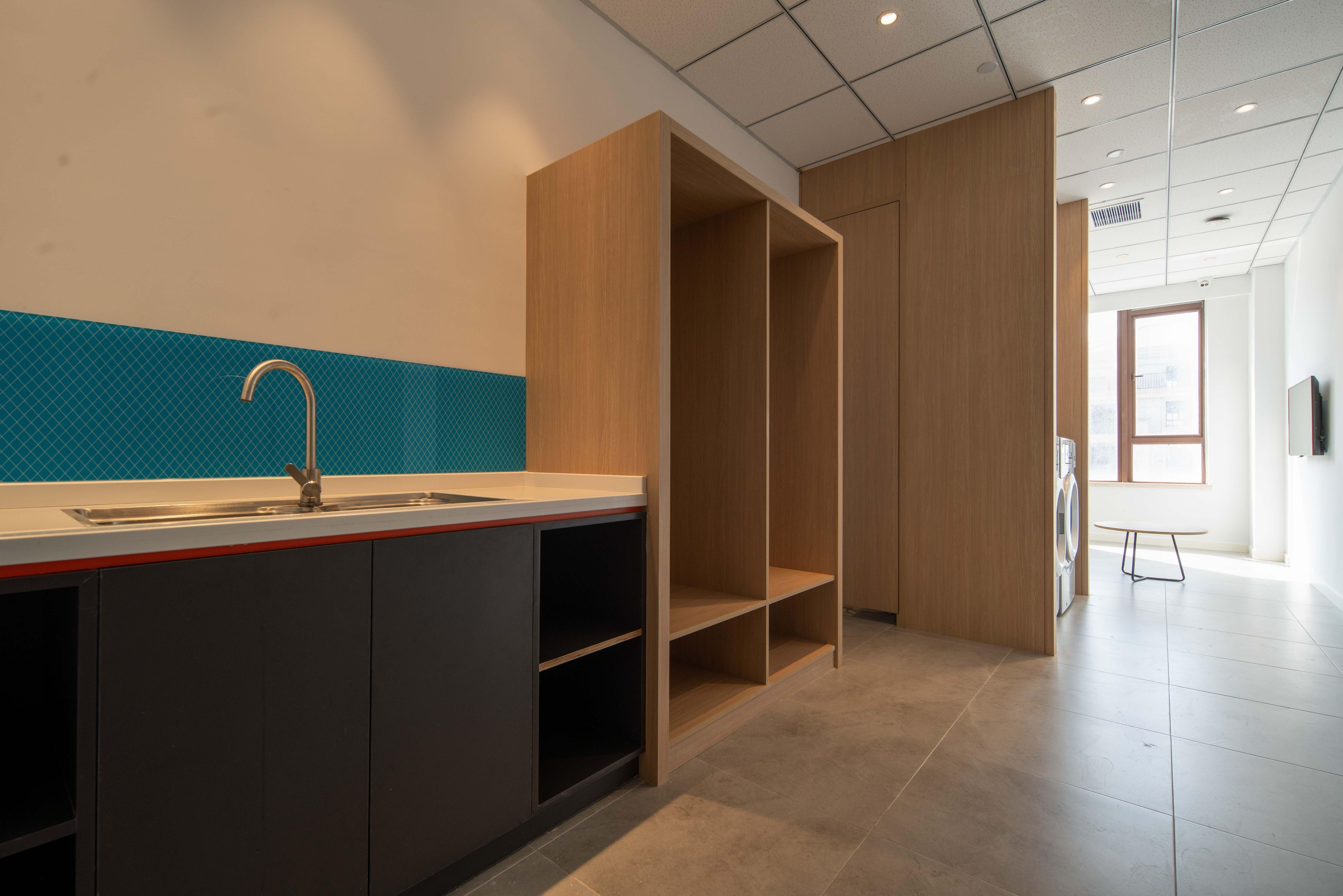 A modern kitchen with a sink, cabinets, and a countertop. There is a wooden cabinet and a window in the background.