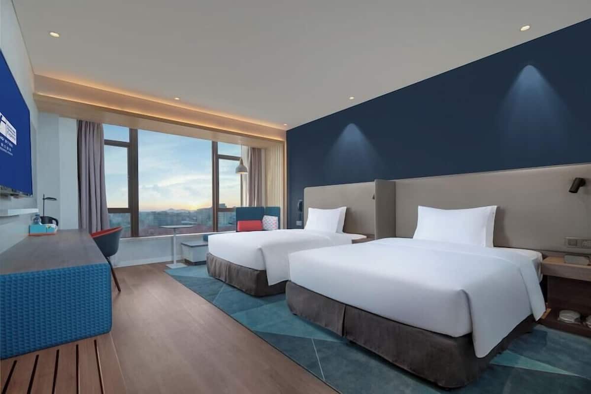 Una habitación de hotel con dos camas, un escritorio, una silla y vistas a la ciudad.