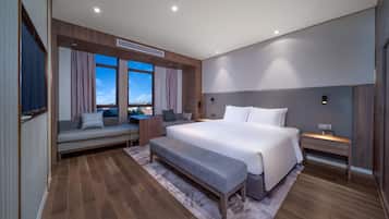 Moderni hotellihuone, jossa on suuri sänky, sohva, penkki ja näkymä kaupunkiin.