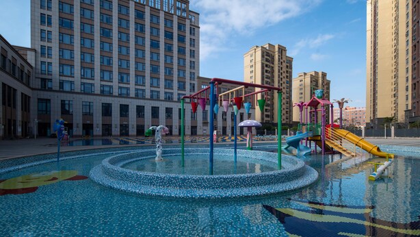 Uma área de recreação infantil com uma fonte circular, escorregadores e estruturas de escalada.