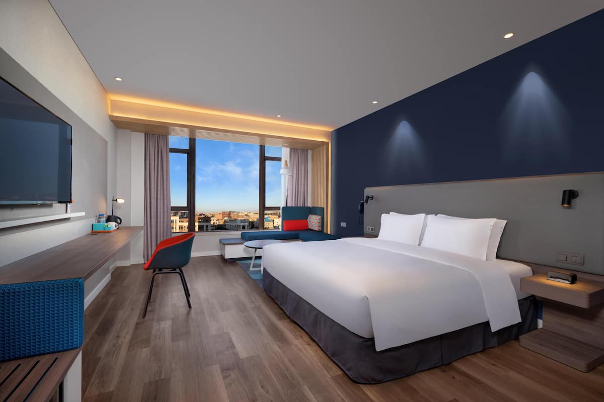Habitación de hotel moderna con una cama grande, un escritorio, una silla y vistas a la ciudad.