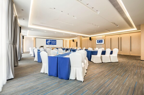 A conference room with rows of tables and chairs, a projector screen, and a sign indicating the hotel's name. - Holiday Inn Express Jinjiang Anhai (Quanzhou)