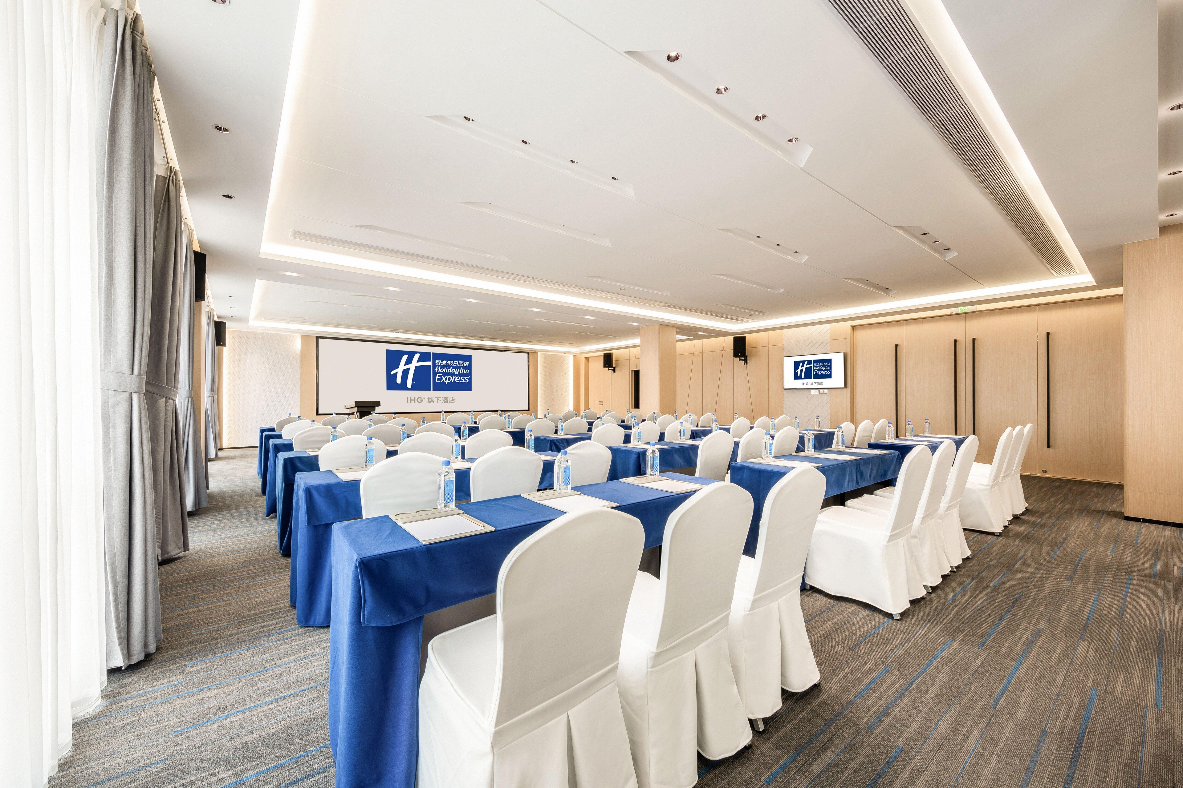 A conference room with rows of tables, white chairs, and a blue tablecloth.
