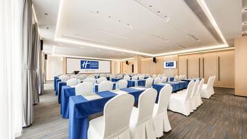 A conference room with rows of tables, white chairs, and a blue tablecloth.