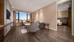 A modern living room with a sofa, armchair, and coffee table, large windows with a city view, and a wooden floor. - Holiday Inn Express Jinjiang Anhai (Quanzhou)