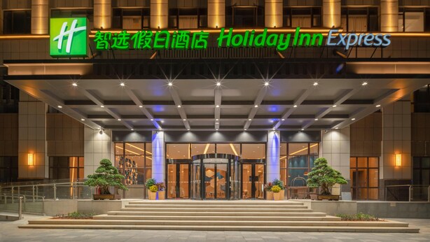 A Holiday Inn Express building with a prominent green logo, a covered entrance, and a well-lit facade. - Holiday Inn Express Jinjiang Anhai (Quanzhou)