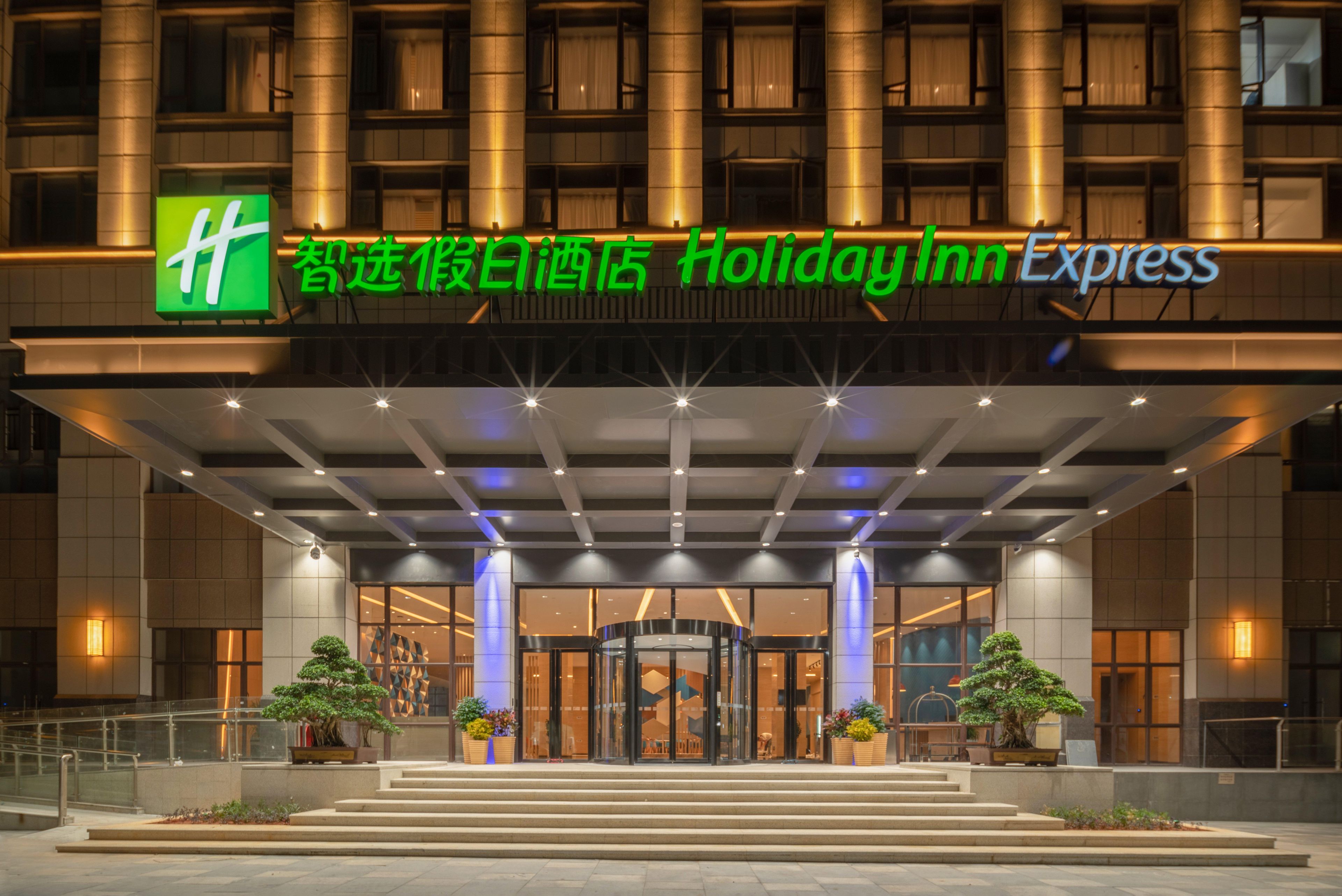 Edifici de Holiday Inn Express amb un logotip verd destacat, un vestíbul cobert i una façana ben il·luminada.