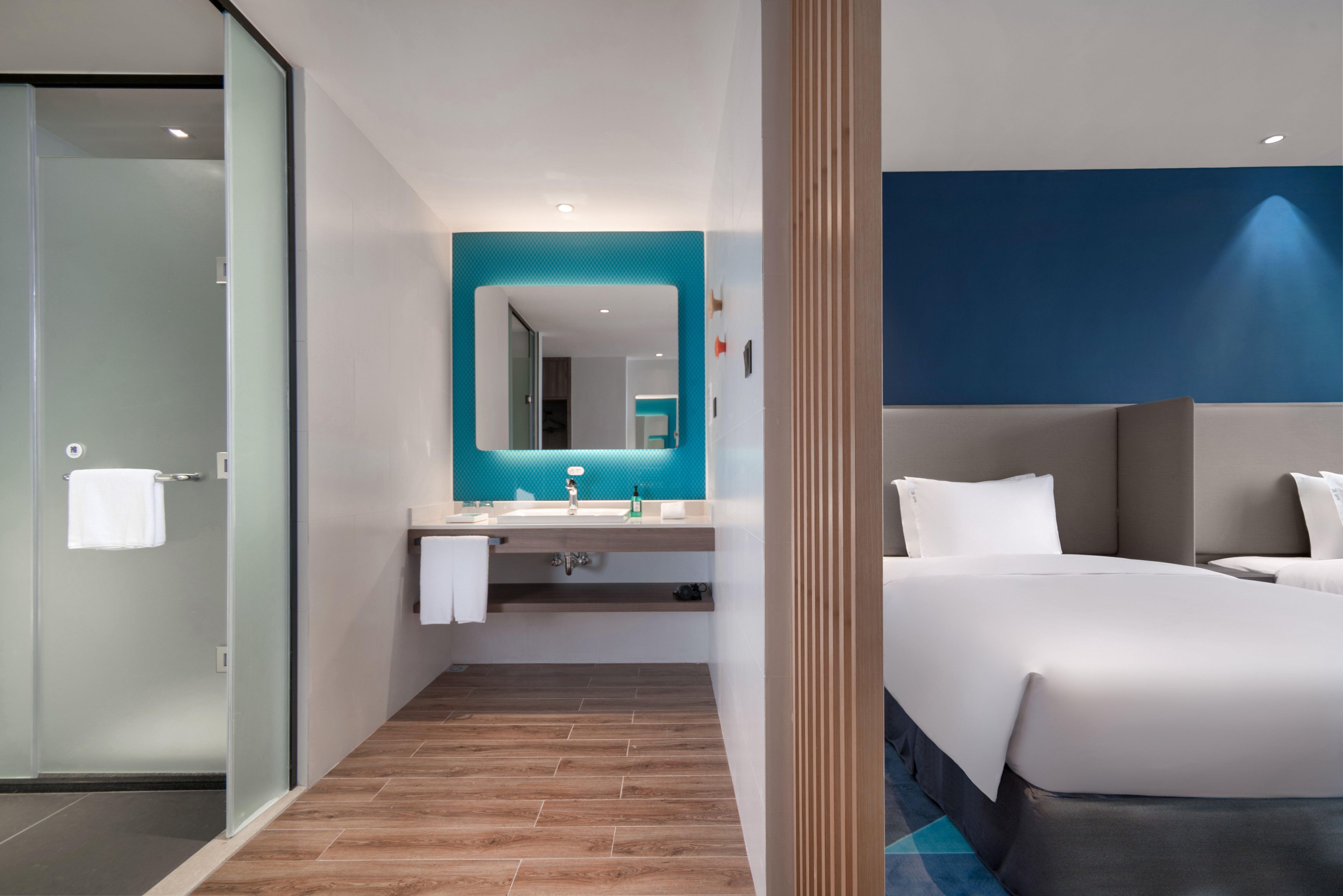 Una habitación de hotel moderna con ducha de vidrio, un espejo grande, una cama y un tocador de baño.