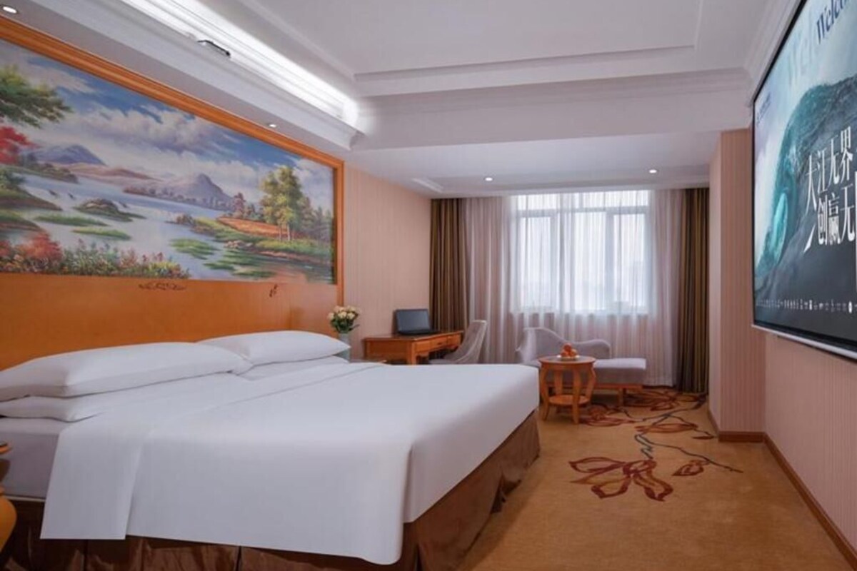 A hotel room with a large bed, a desk, a chair, a TV, and a mural on the wall.