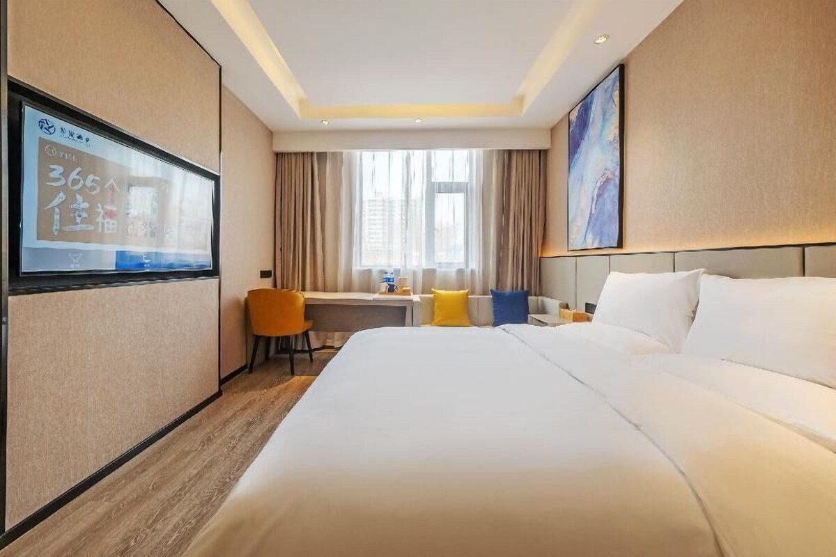 A hotel room with a bed, a desk, a chair, a TV, and a window with curtains.