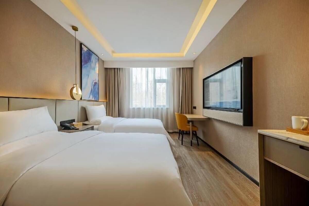 A hotel room with two beds, a desk, a chair, a TV, and a painting on the wall.