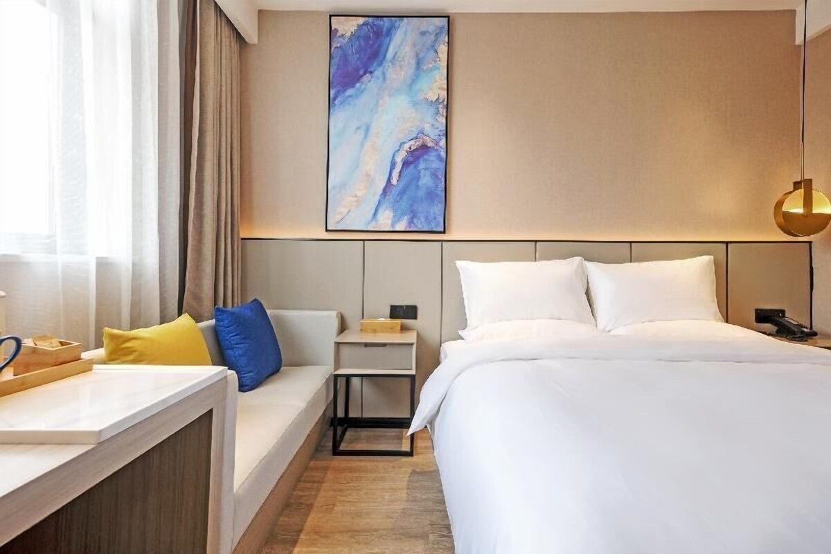A hotel room with a bed, bedside table, lamp, and a painting on the wall.