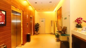 A hotel lobby with wooden paneling, an elevator, a reception desk, a door, and a potted plant. - Jinjiang Inn Select Hotel (Wuhan)