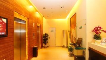 Um saguão de hotel com lambris, um elevador, um balcão de recepção, uma porta e um vaso de plantas.