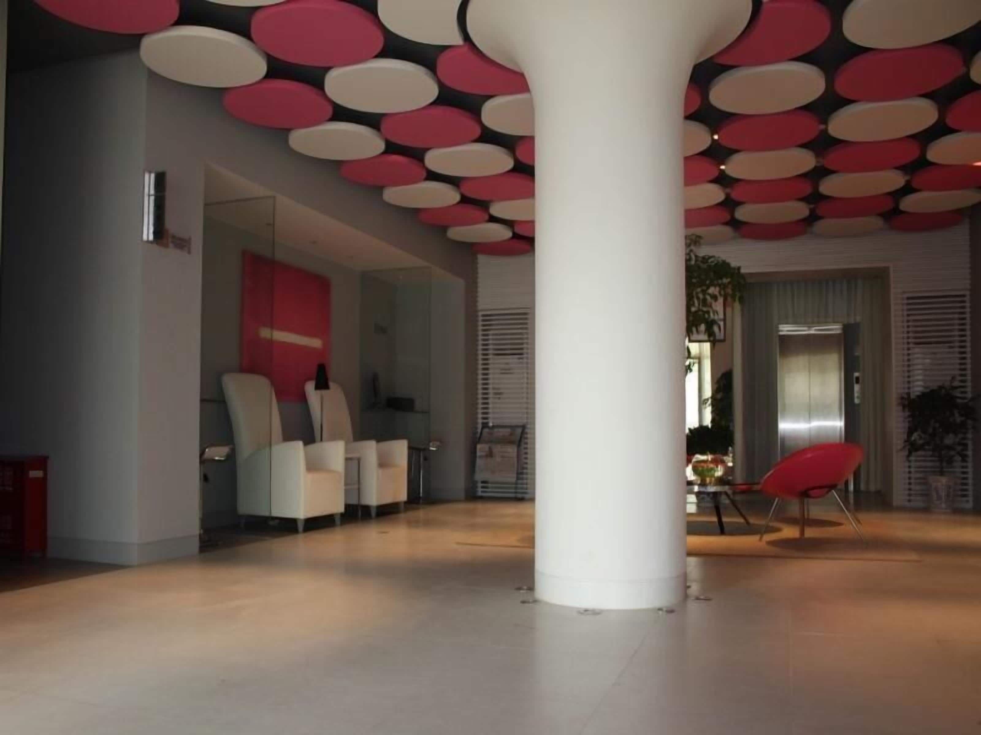 Um hall amplo com design moderno, apresentando uma coluna branca grande, áreas de estar e um elevador visível.