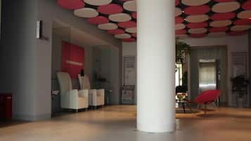 Um hall amplo com design moderno, apresentando uma coluna branca grande, áreas de estar e um elevador visível.