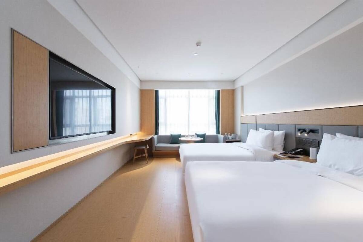 A hotel room with two beds, a desk, a chair, a window, and a bedside table.