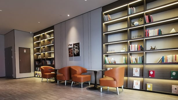 Una biblioteca moderna con estanterías, sillones de cuero y suelo de madera.