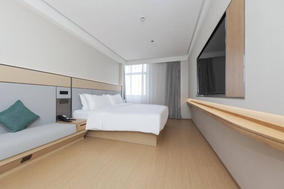 Une chambre d’hôtel avec un lit, un canapé, une table de chevet, un miroir et une fenêtre avec des rideaux.