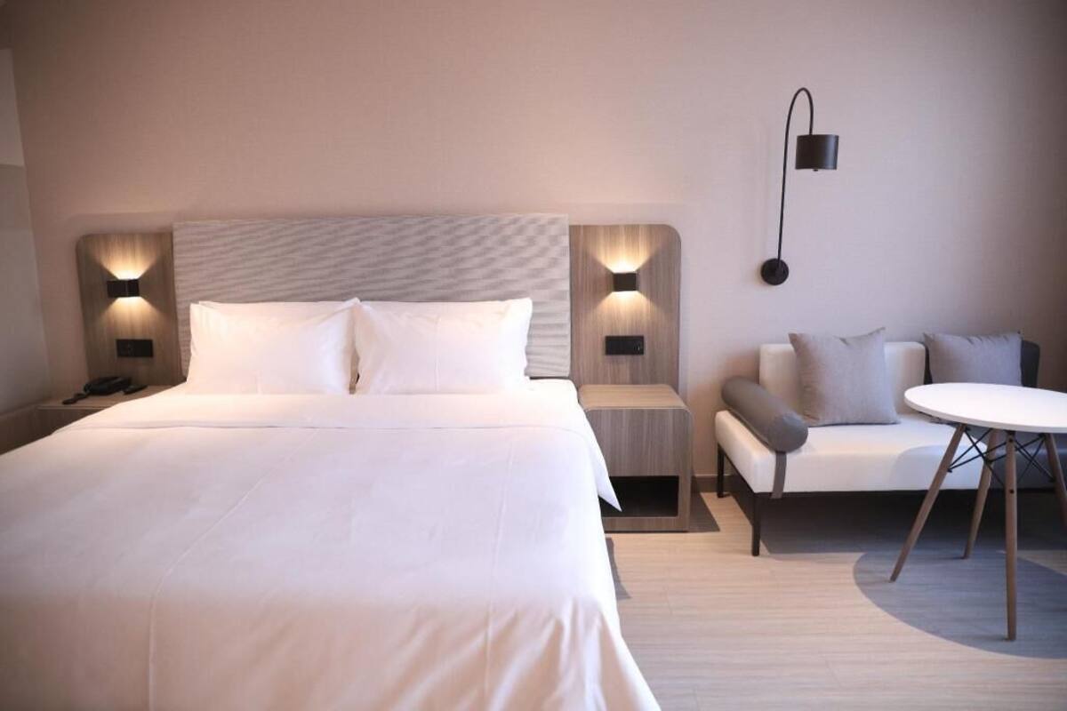 A hotel room with a large bed, bedside tables, a sofa, and a small round table.