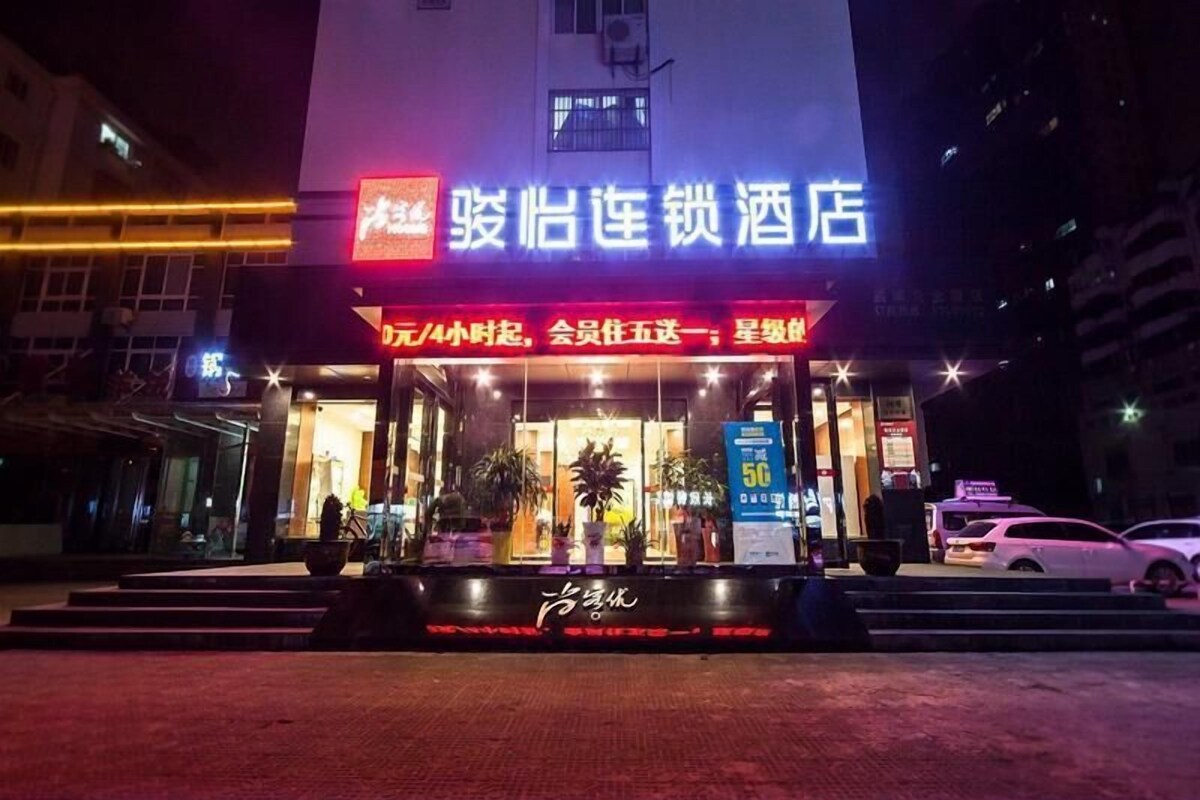 A hotel entrance with a neon sign, a glass facade, and a staircase leading up to the door.