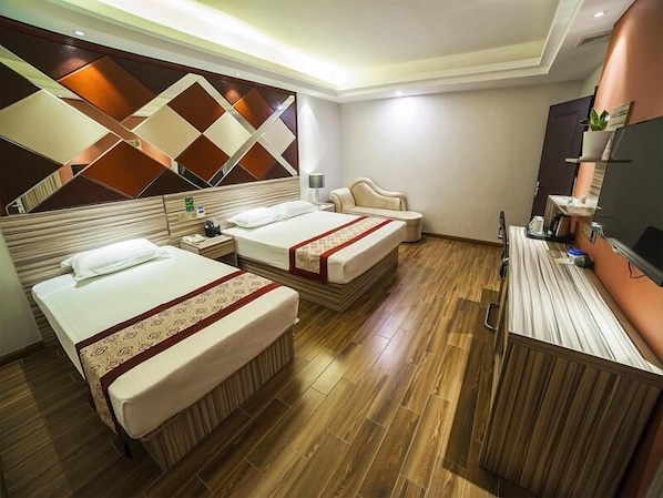 Habitación de hotel con dos camas, piso de madera, televisor y espejo con diseño geométrico en la pared.