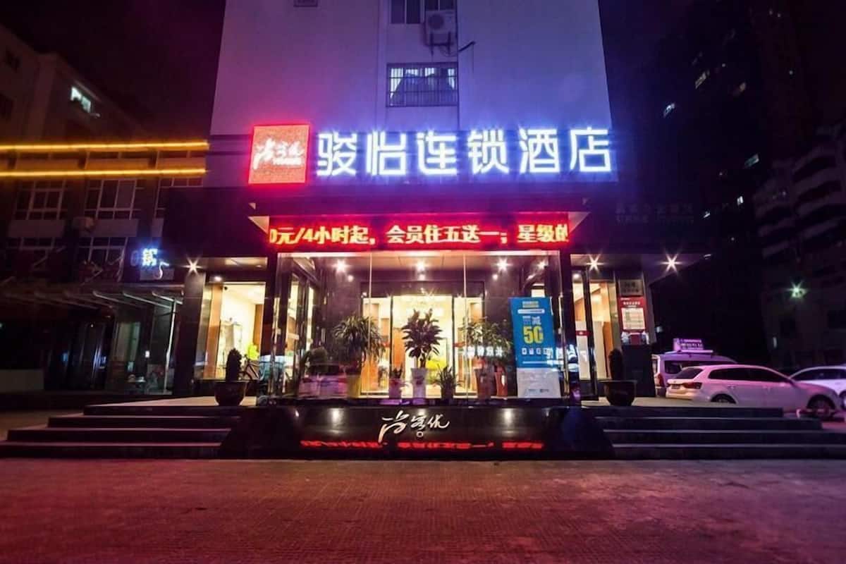 A hotel entrance with a neon sign, a glass facade, and a staircase leading up to the door.
