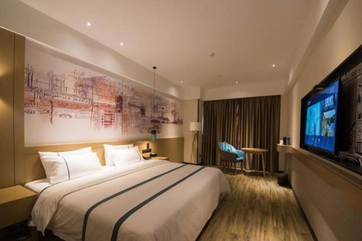 A hotel room with a large bed, a television, a desk, and a wall with a mural.