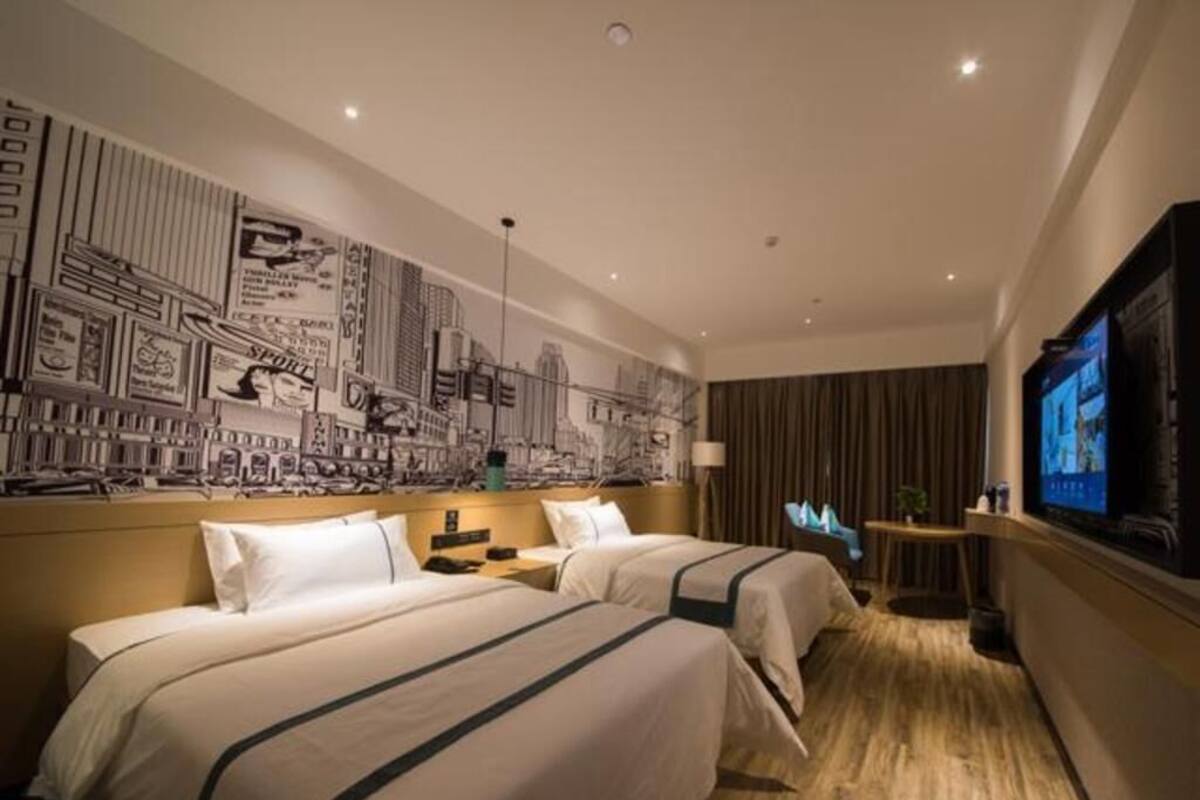 A hotel room with two beds, a cityscape mural, a television, and a wooden floor.