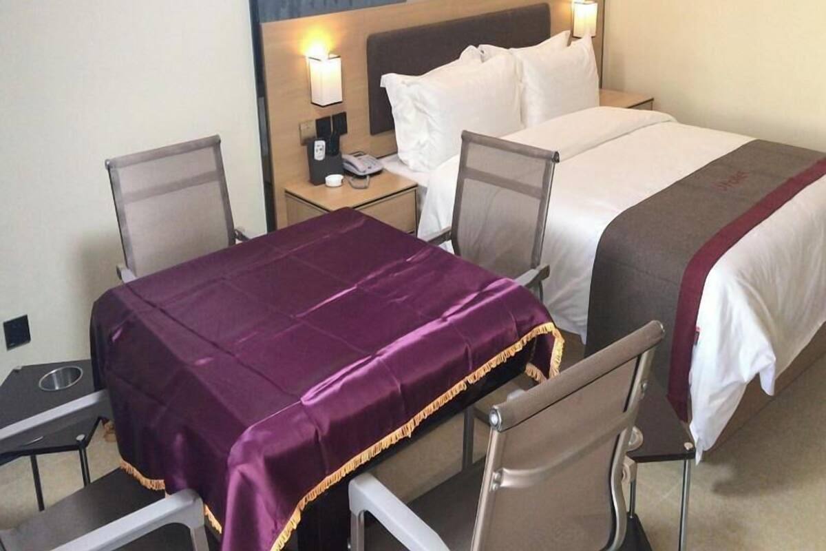 Et hotelværelse med en seng, to stole, et skrivebord med telefon og et natbord med lampe.