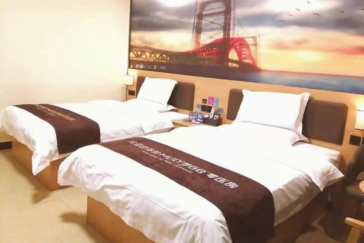 Et hotelværelse med to senge, et stort maleri af en bro og et natbord med genstande.