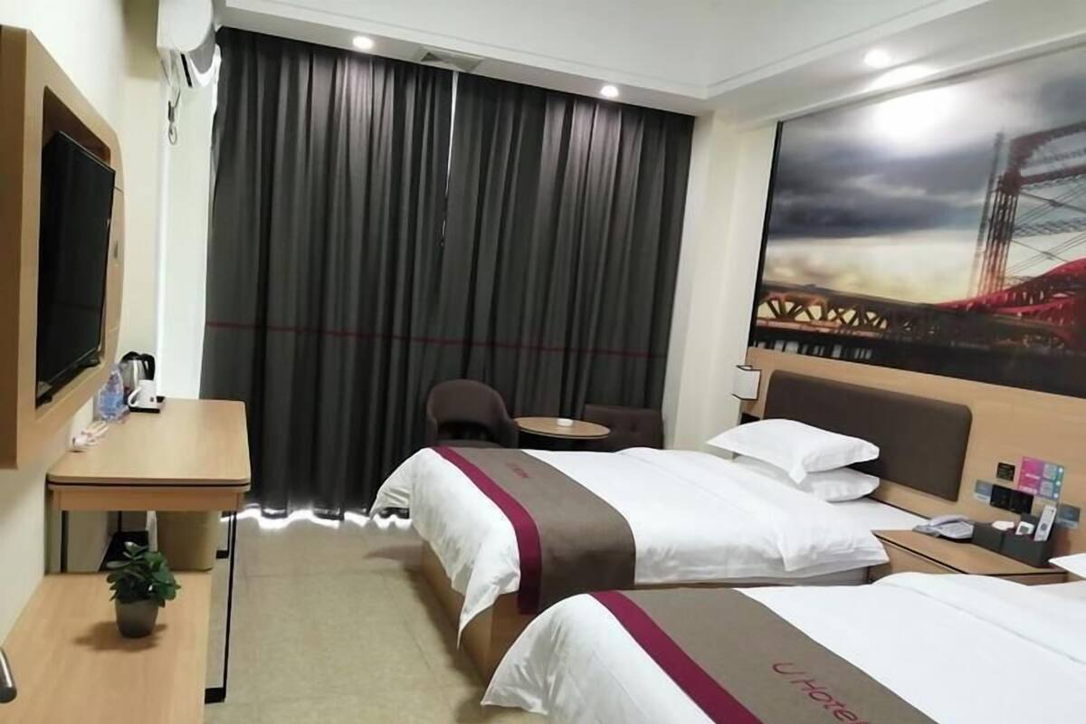Et hotelværelse med to senge, et skrivebord, en stol, et lille bord, et fjernsyn og et maleri af en bro.