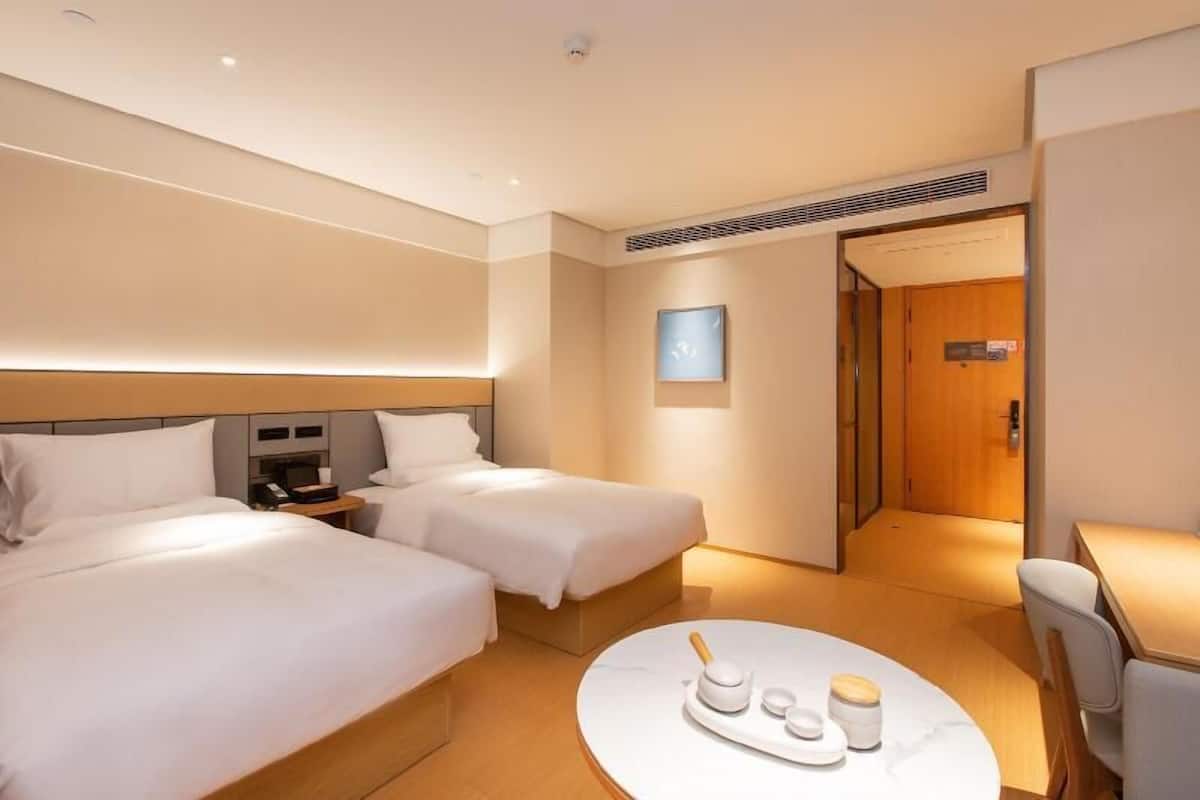 A hotel room with two beds, a bedside table with a phone, a round coffee table with a tray, and a door leading to another room.