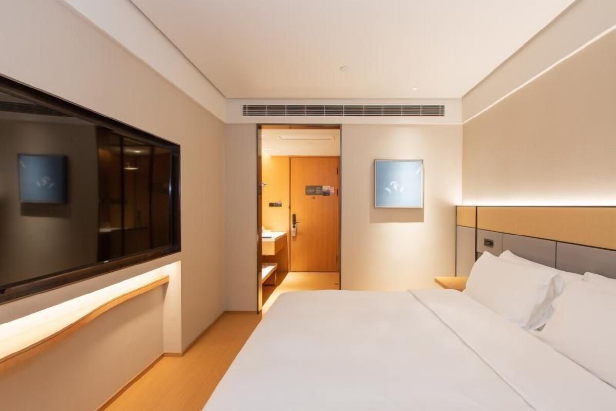 Quarto de hotel com uma cama, televisão, porta para um banheiro e luminária fixada na parede.
