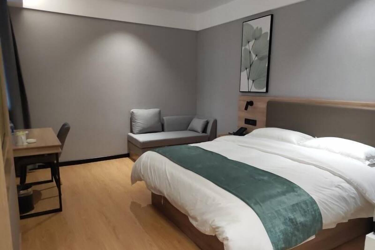 Moderni hotellihuone, jossa on sänky, työpöytä ja oleskelualue.