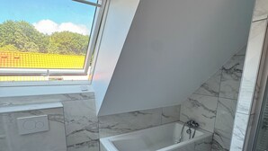 Une salle de bain moderne avec une lucarne, une baignoire et des toilettes.