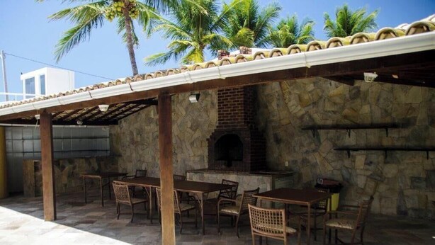 Un patio al aire libre con paredes de piedra, un horno de ladrillo y mesas y sillas de madera.