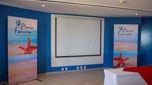 Una habitación con paredes azules, una pantalla de proyector y dos carteles con una estrella de mar y el texto 'Maria Farinha Praia Hotel'.