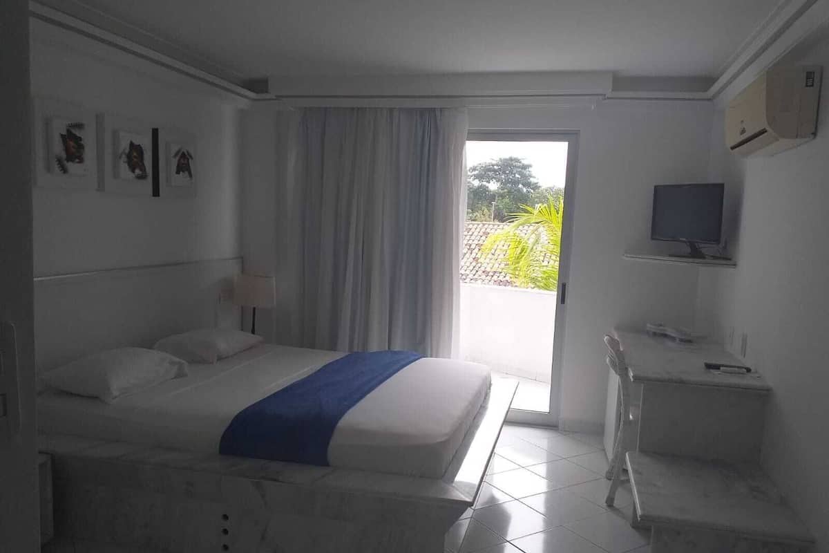 Ein Hotelzimmer mit einem Bett, einem Schreibtisch, einem Fernseher und einem Fenster mit Vorhängen.