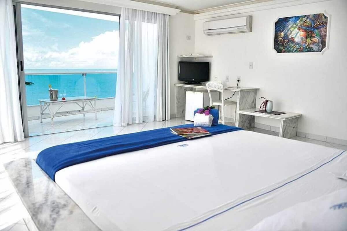 Ein Hotelzimmer mit Bett, Fernseher, Schreibtisch, Stuhl, kleinem Tisch und Meerblick.