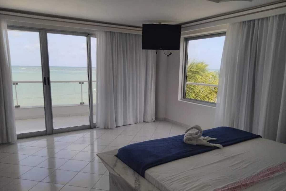 Ein Hotelzimmer mit Bett, Fernseher, Meerblick und einem Balkon.