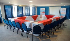 Un salón de conferencias con mesas, sillas, una pantalla de proyector y un cartel.