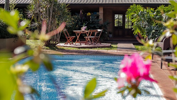 A swimming pool with a patio area, surrounded by lush greenery and a brick building. - El Descanso Iguazú by DOT Cabana (Puerto Iguazú)