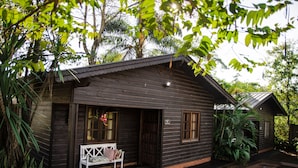 A wooden cabin with a porch, a bench, and a small garden area. - El Descanso Iguazú by DOT Cabana (Puerto Iguazú)