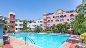 A swimming pool surrounded by a building with balconies and a clear blue sky.