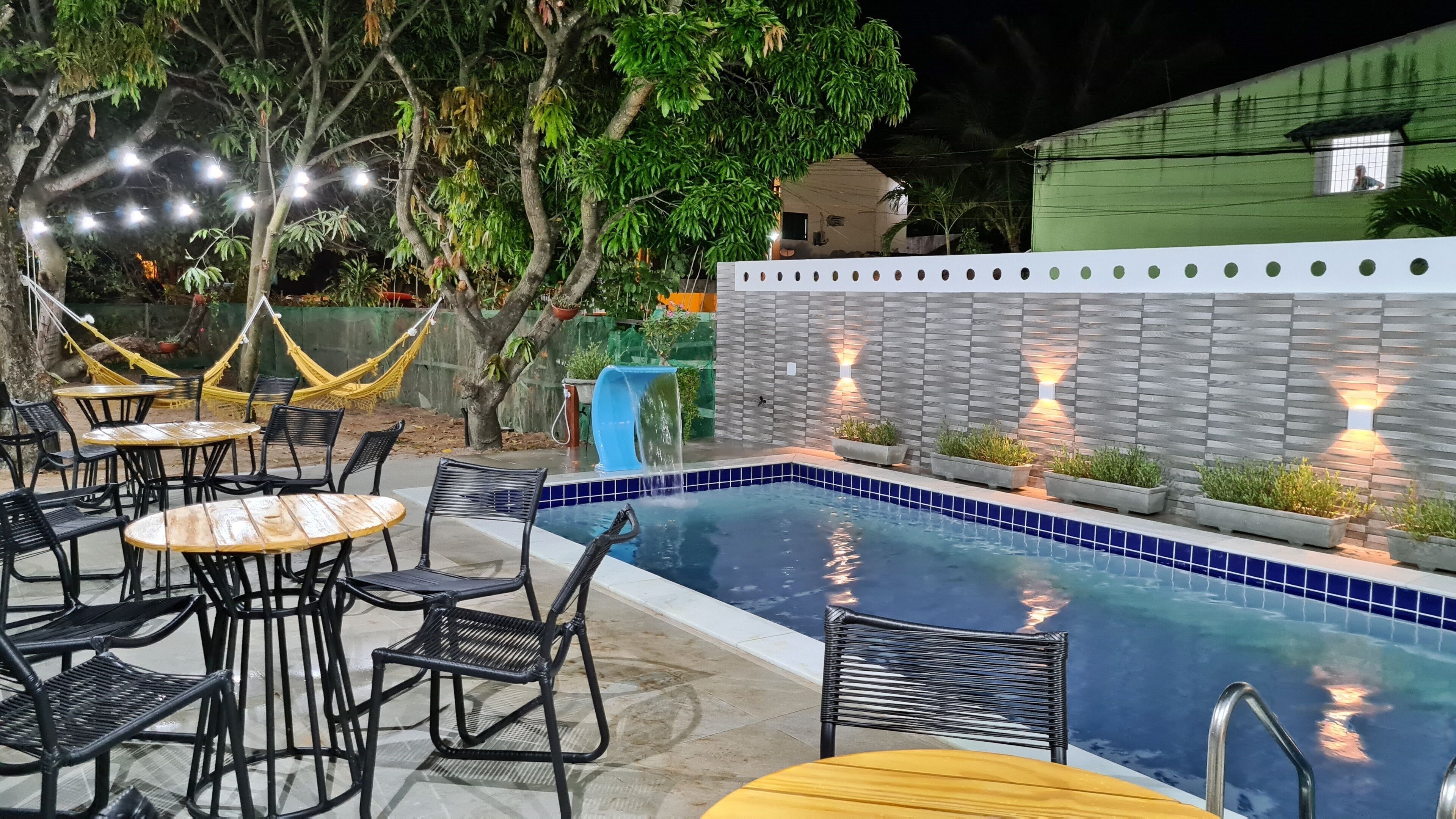 Un área de piscina al aire libre con mesas y sillas, una hamaca y una pared con luces.