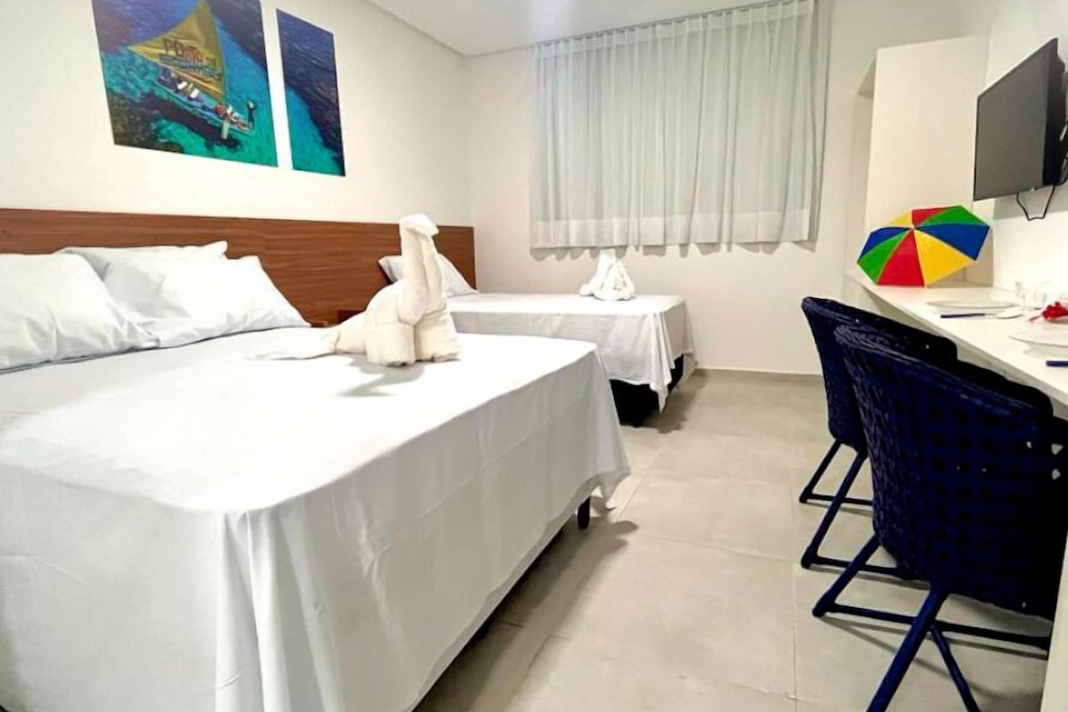 Une chambre d’hôtel avec deux lits, un bureau avec un ordinateur, une télévision et des œuvres d’art accrochées au mur.