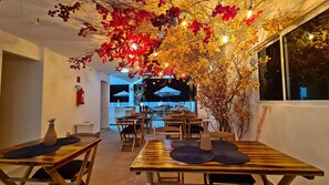 An indoor dining area with wooden tables and chairs, a fire extinguisher on the wall, and a view of the outdoor seating area. - Porto Sol Vila By Aft (Ipojuca)